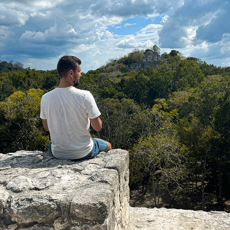 Mann auf Mauer mit Maya Ruine im Hintergrund