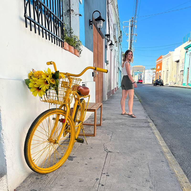 gelbes Fahrrad auf Straße mit Frau im Hintergrund