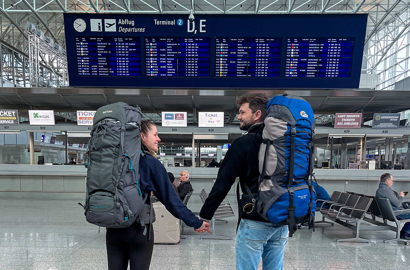 Paar am Flughafen mit Rücksäcken hält Händchen