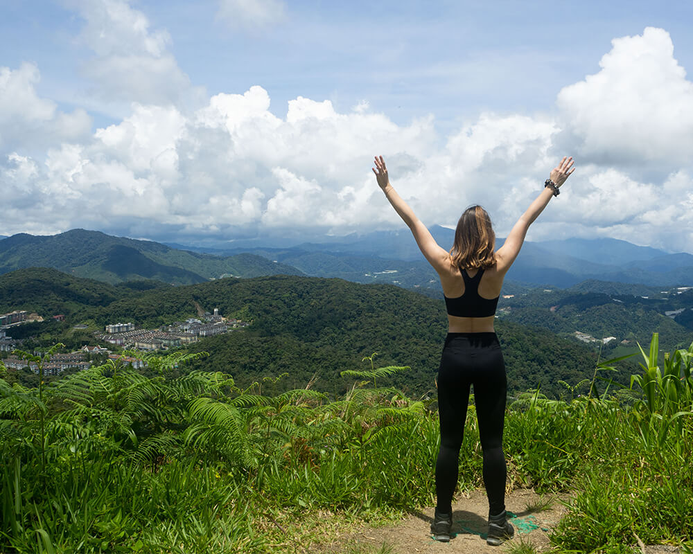 Frau steht auf Berg in Cameron Highlands und streckt die Arme nach oben