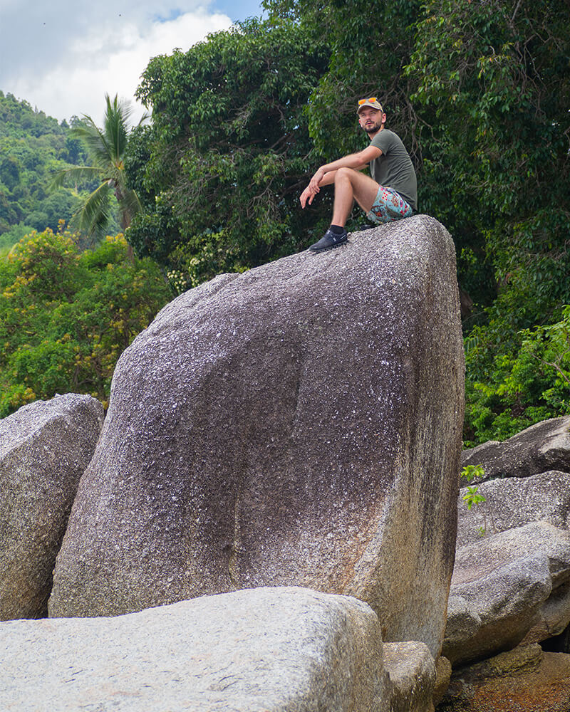 Mann sitzt auf einem sehr großen Stein