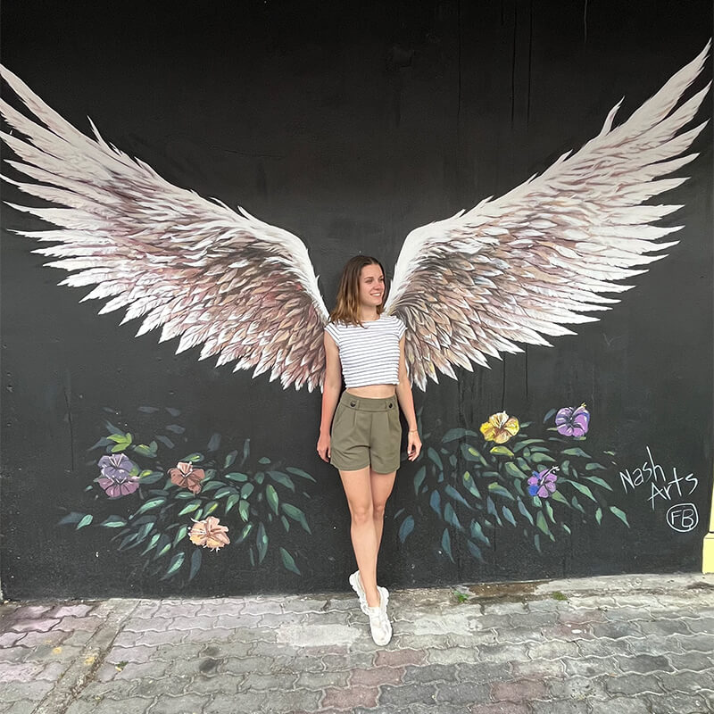 Frau steht vor einem Wandgemälde mit Flügeln