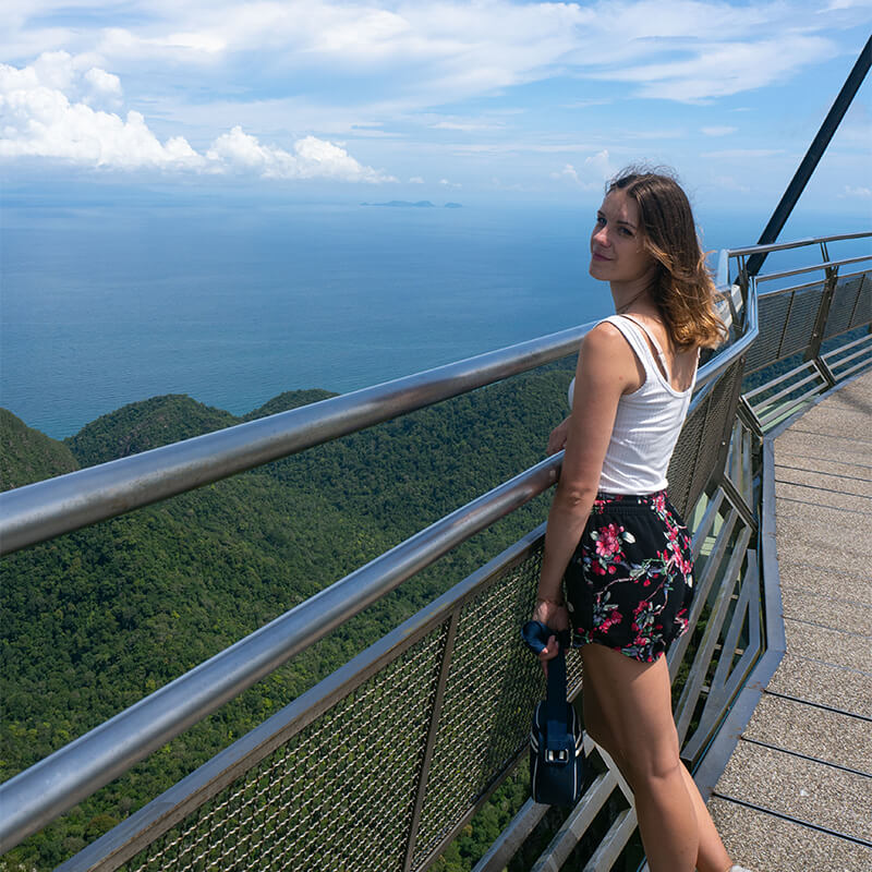 Frau steht auf Brücke mit Ausblick auf Regenwald und Meer