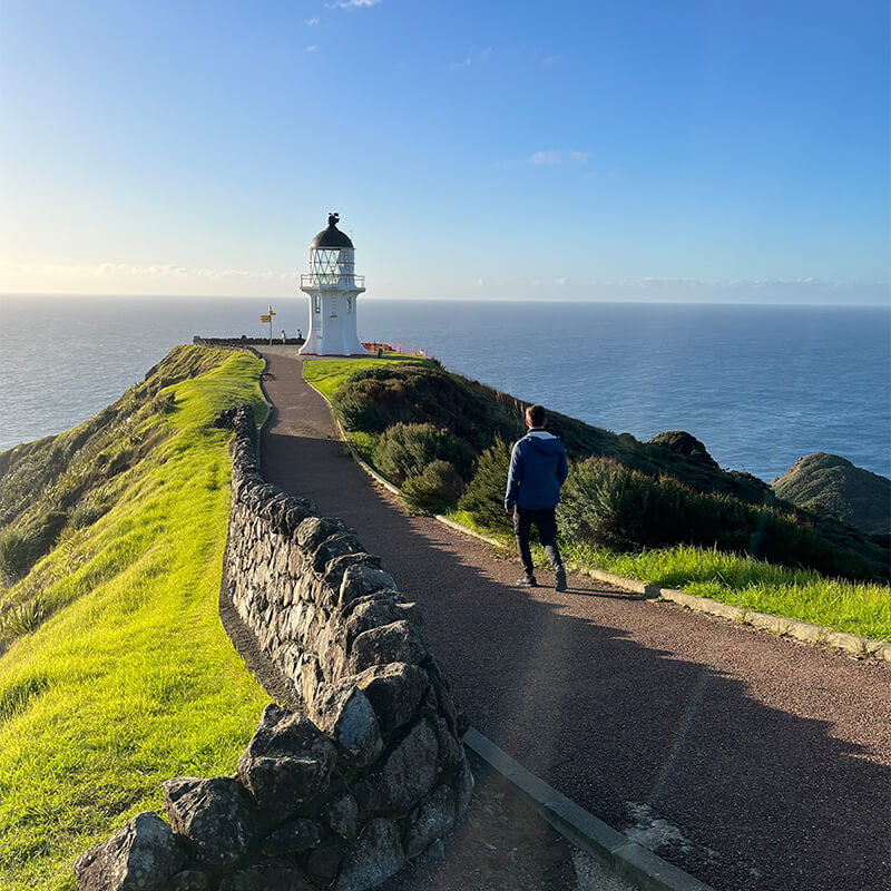 Mann läuft einen Weg zu einem Leuchtturm an der Küste