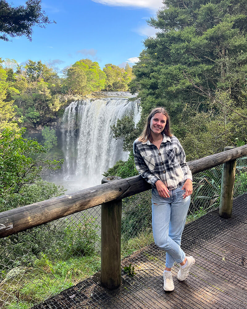 Junge frau steht vor einem Geländer mit einem Wasserfall im Hintergrund