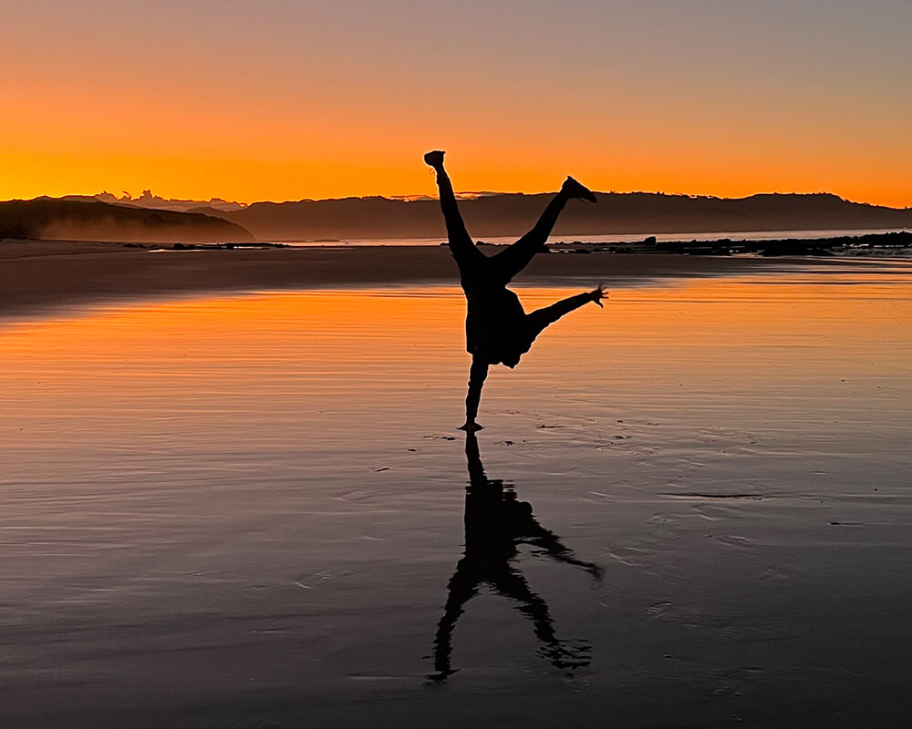 Silhouette eines Mannes bei untergehender Sonne, der einen Handstand auf dem Strand macht