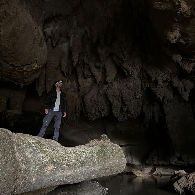junger Mann mit Stirnlampe steht auf einem großen Stein in einer Höhle 