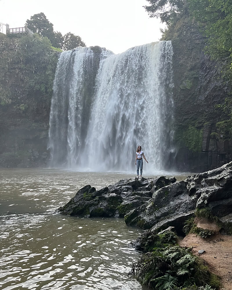 junge Frau steht auf einem Stein vor dem Whangarei Wasserfall 