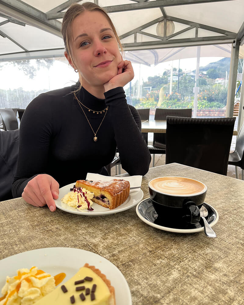 junge Frau mit Rollkragenpullover sitzt vor einem Stück Kuchen und Kaffetasse