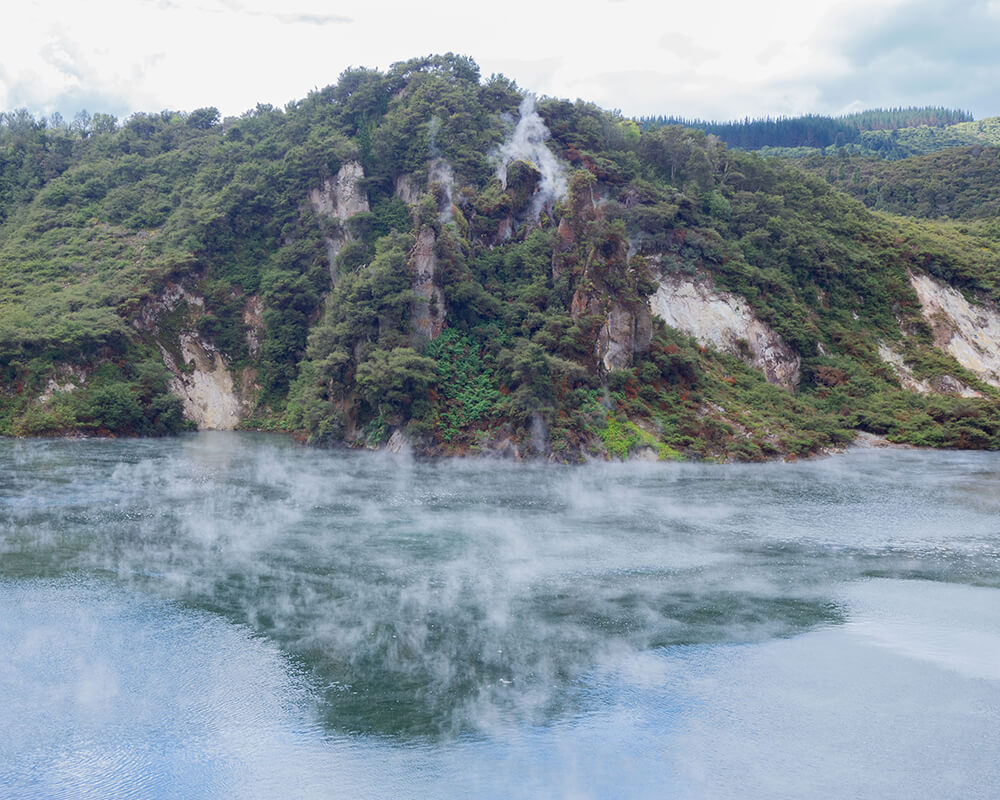 See mit Rauch vor einem felsigen Berg