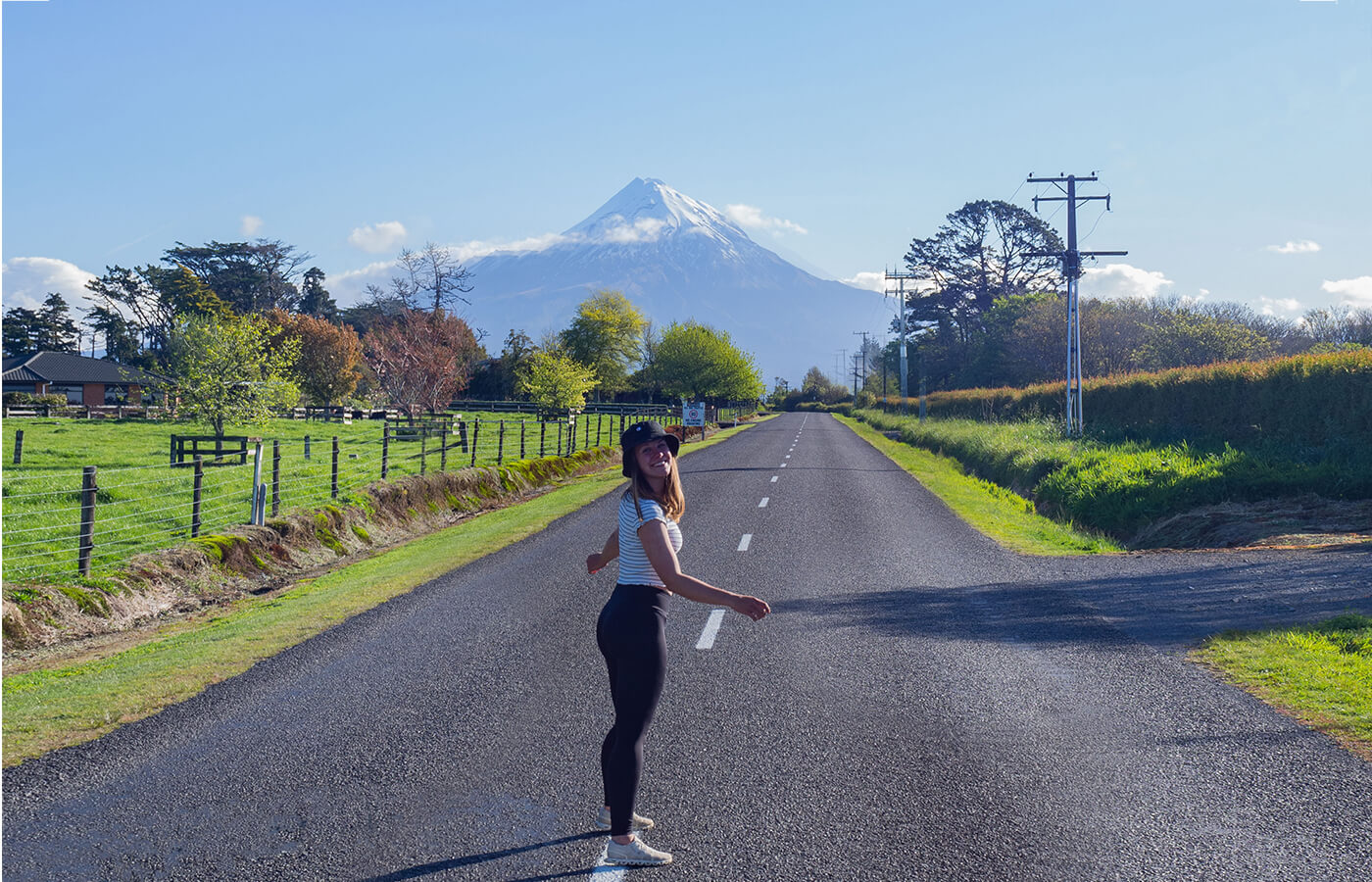 Junge Frau steht auf einrer Straße, im Hintergrund sieht man den Mount Taranaki