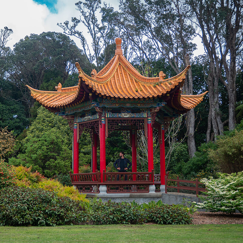 junger Mann steht in einem kleinen, orang-rotem chinesisch aussehenden Pavillon