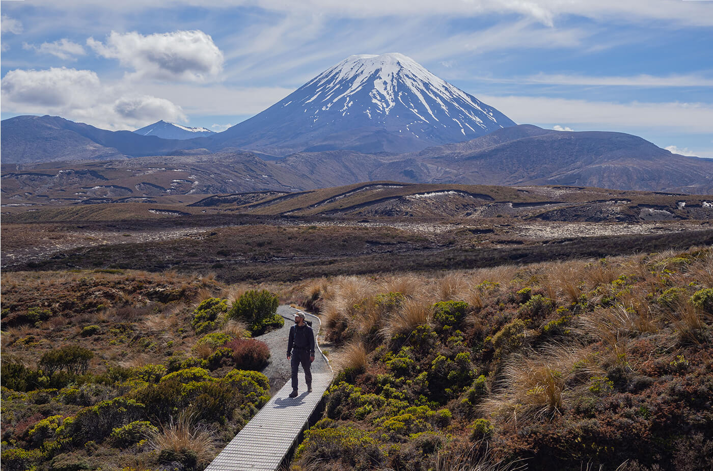 Junger Mann läuft auf einem Holzweg durch eine Trockene Landschaft, im Hintergrund ist ein Vulkan
