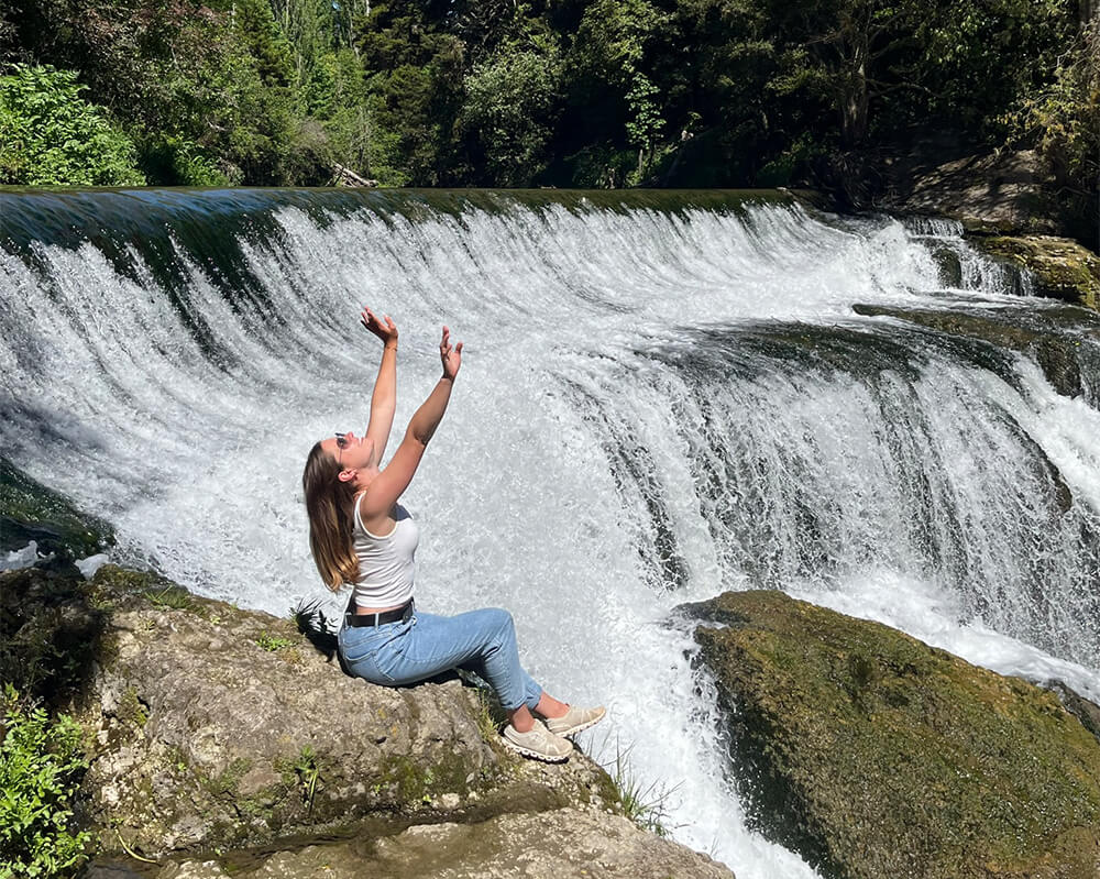 junge Frau sitzt auf einem Felsen vor einem Wasserfall