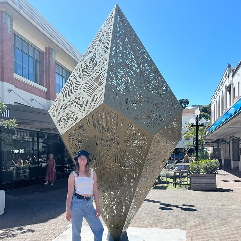 junge Frau steht vor einem Diamatförmigem Skulptur