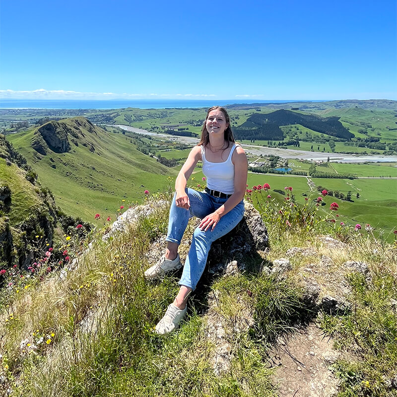 junge Frau sitzt auf einem Hügel mit einer grünen Landschaft im Hintergrund