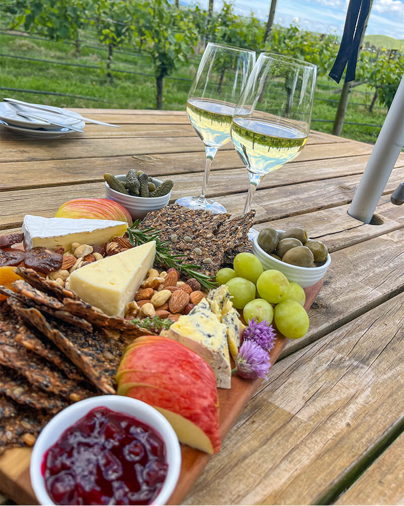 Käseplatte mit Obst und zwei Weingläsern steht auf einem Tisch mit Weinbergen im Hintergrund
