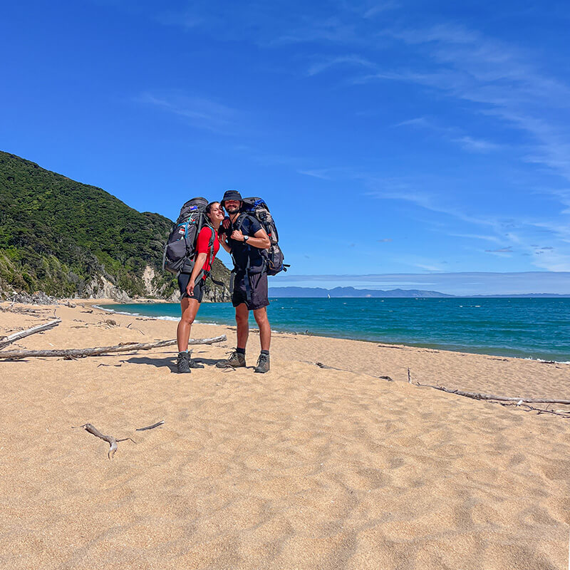 junges Paar mit großen Rucksäcken steht am Strand