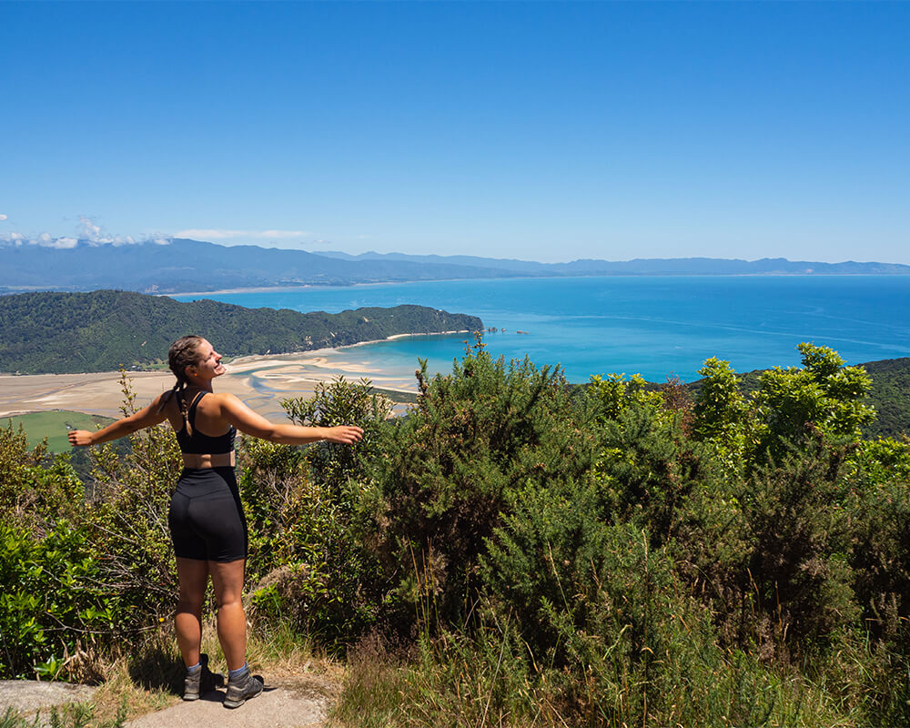 junge Frau in Wanderkleidung, im Hintergrund eine Bucht und Wald