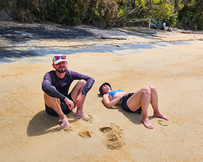 junger Mann sitzt am Strand, nehmen ihm liegt eine junge Frau