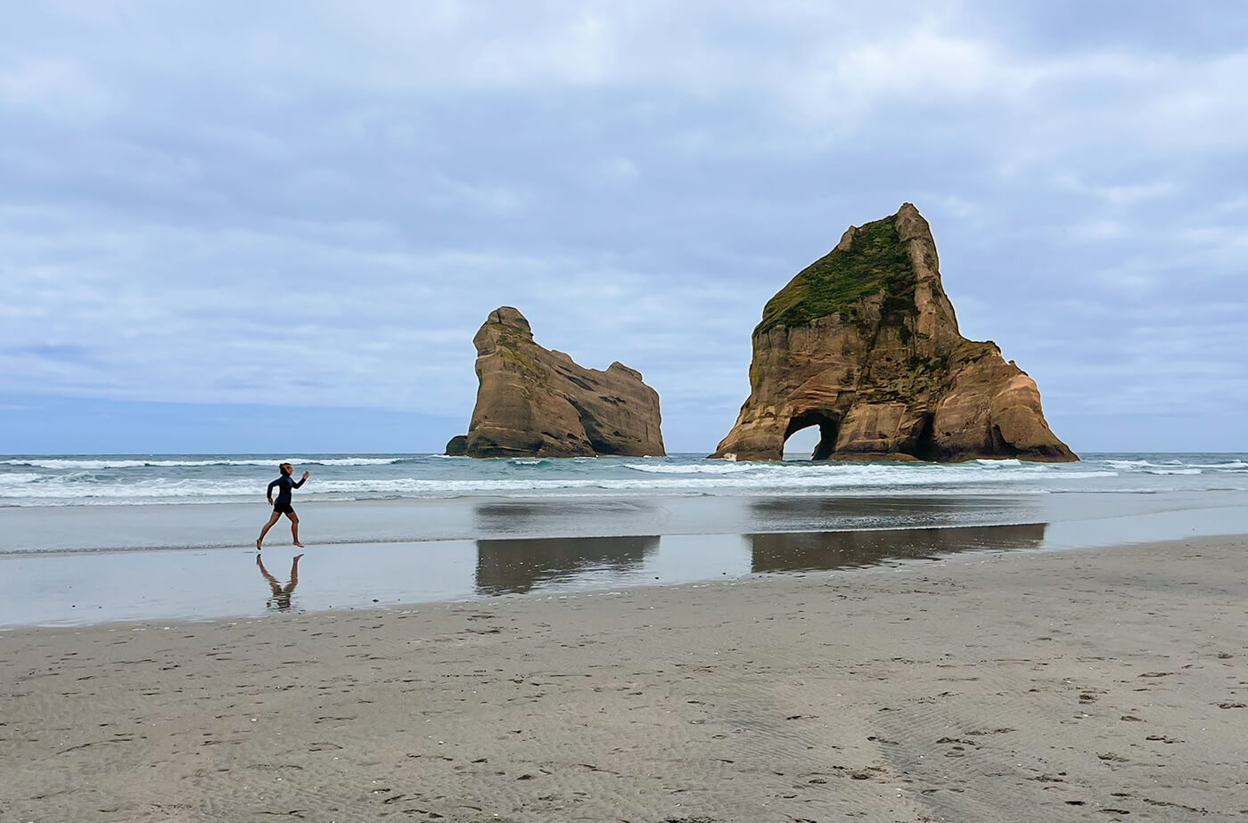 Frau joggt am Strand entlang, im Hintergund sind Felsen