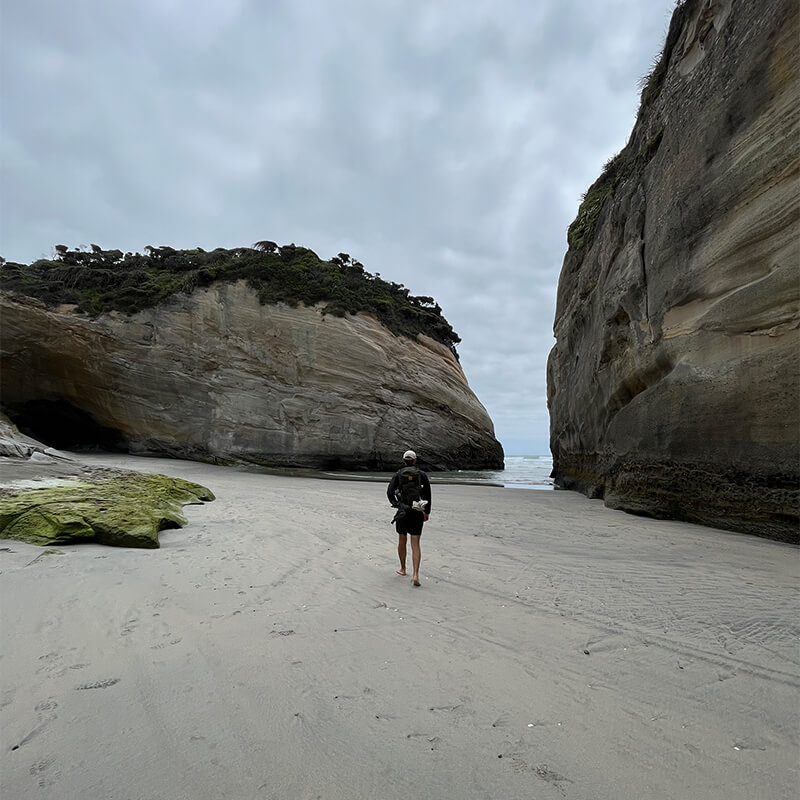 junger Mann läuft am Strand zwischen Felsen hindruch