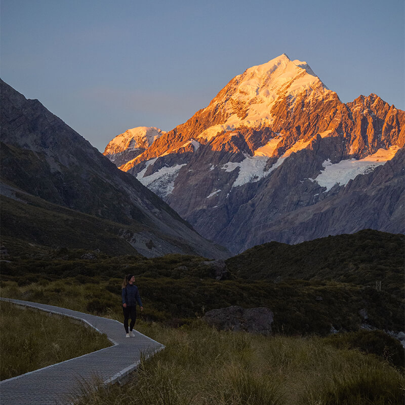 junge Frau steht auf Wanderweg mit Mout Cook in Hintergrund