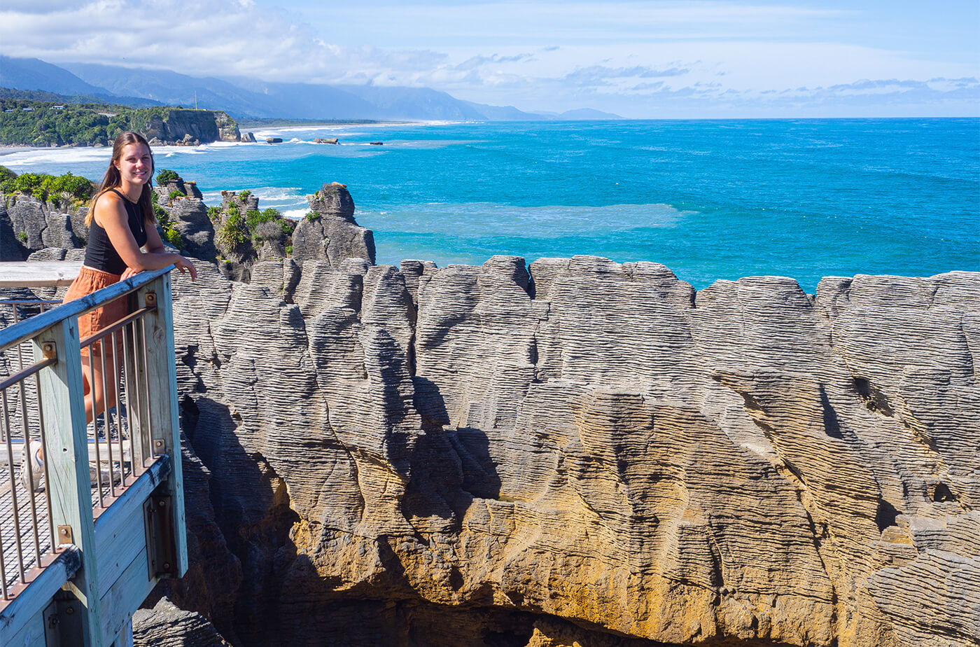 Junge Frau lehnt an einem Geländer und schaut auf die Pancake Rocks