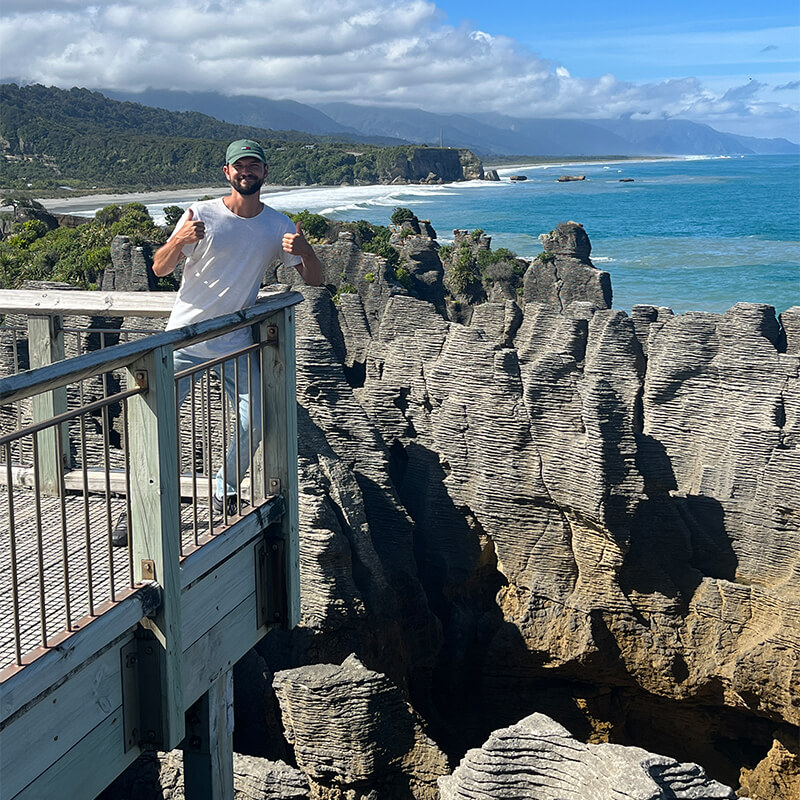 junger Mann steht auf einer Plattform  mit Geländer an den Pancake Rocks
