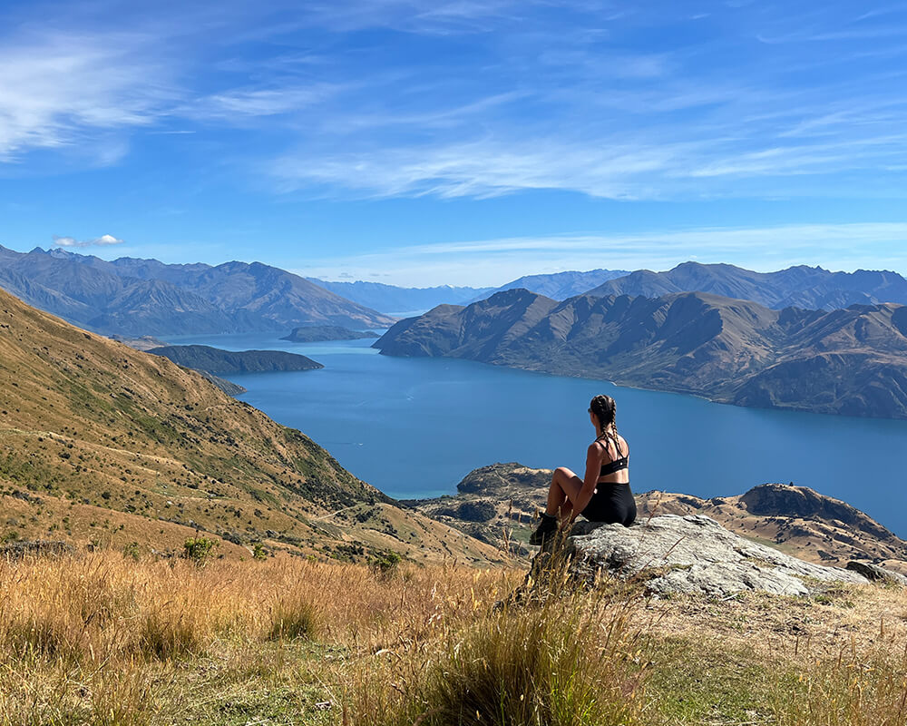 Frau sitzt auf einem Felsen, im Hintergrund ist der Wanaka Lake